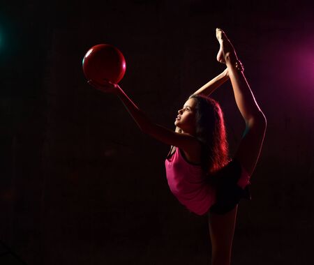 Young athletic girl gymnast doing rhythmic gymnastic exercises performing vertical splits stretching...