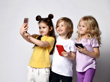 Young children take selfie with mobile phone broadcast online hold cellphones in hands on white backgroundの写真素材