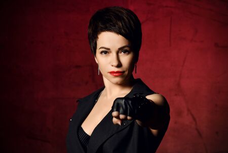 Portrait of self-confident brutal brunette woman in leather gloves with cut fingers punches ready to fight over dark red backgroundの写真素材