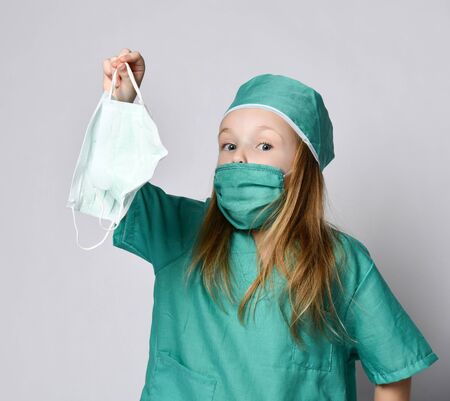 Little girl child play doctor in green medical coat hold  protection masks from the Coronavirus...