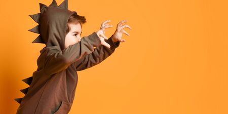 Cheerful kid boy in green hoodie with dinosaurus spikes at his back and cowl playing t-rex beast...