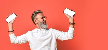 Stylish smiling grey-haired hipster adult man in white hoodie and sunglasses standing holding...