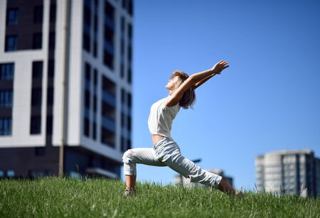 Young woman doing yoga stretching exercises at the modern city park on a blue sky backgroundの写真素材