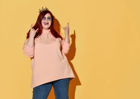 Young smiling red haired overweight woman in casual clothing, sunglasses and golden crown on head...
