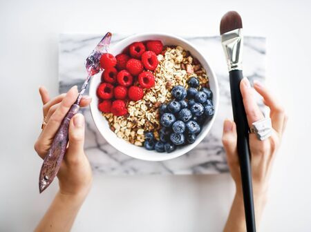 Art concept design breakfast. Artist painter hands hold palette knife and paint brush ready to eat cereal porridge with berries fruits fresh raspberry and blueberry on marble backgroundの写真素材