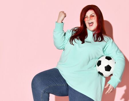 Pretty young plus size woman in jeans, blue hoodie and sunglasses standing with ball holding hand...