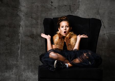 Smiling kid girl in winter fur jacket sitting with her hands spread up like holding something surprised on her open palms with copy object space overの写真素材