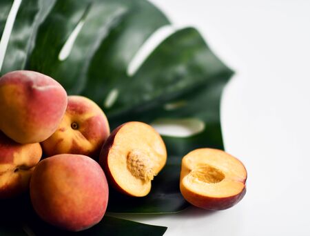 Whole and halved fresh peaches on large palm tree leaf background with free text copy space. Organic superfood concept for healthy eatingの写真素材