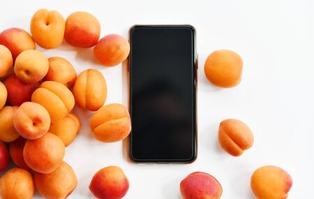 Big fresh apricots scattered around smartphone blank screen background with free text copy space. Organic superfood concept for healthy eatingの写真素材