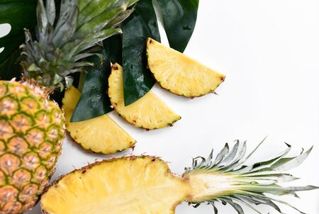 Fresh whole halved and sliced pineapple at big tropical leaf over white background with free text...