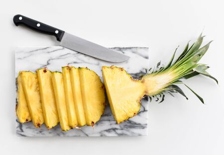 Freshly halved and sliced juicy pineapple and knife on marble slab board over white background. Organic superfood concept for healthy eatingの写真素材
