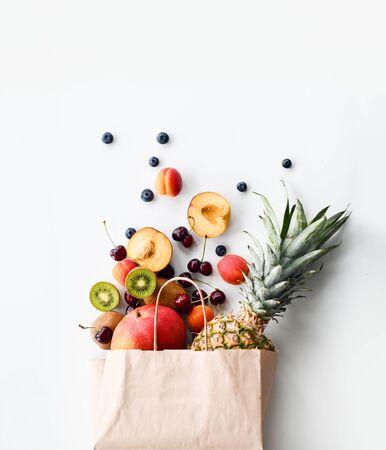 Fruits and berries delivery composition in paper shopping bag blueberry raspberry cherries kiwi pineapple mango apricot on white background with free text copy spaceの写真素材