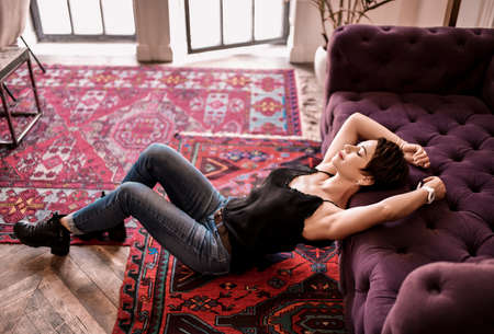 Smiling relaxing dreaming short haired brunette woman in black shirt, jeans and brutal shoes sits on...