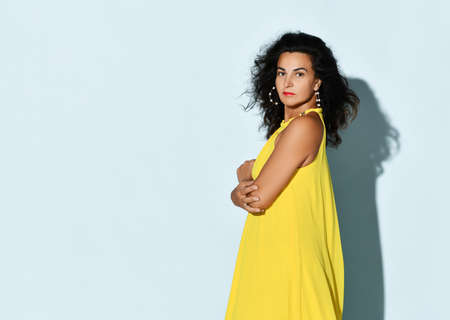 Romantic woman fashion model wearing stylish summer yellow dress studio headshot portrait on blue...