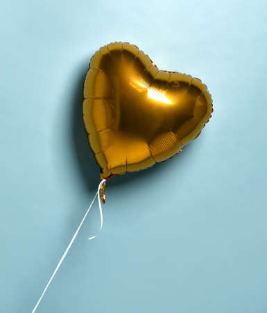 Metallic foil single gold heart balloon baloon object for birthday party or valentines day on pastel color light blue backgroundの写真素材
