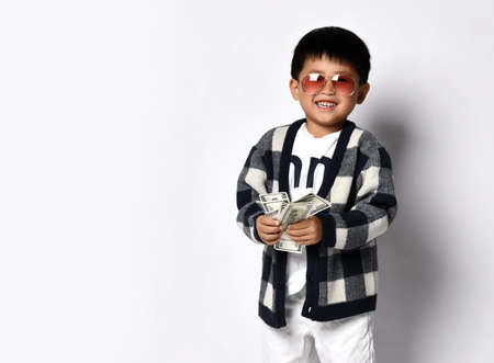Happy asian rich kid boy millionaire in modern sunglasses,  plaid cardigan and white pants stands...