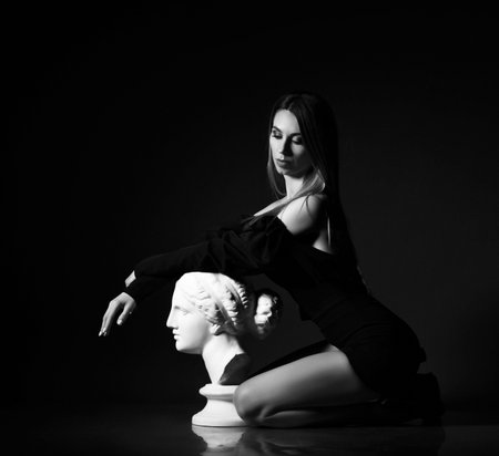 Young beautiful sexy woman in black dress sitting with eyes closed and holding hands on sculpture profileの写真素材