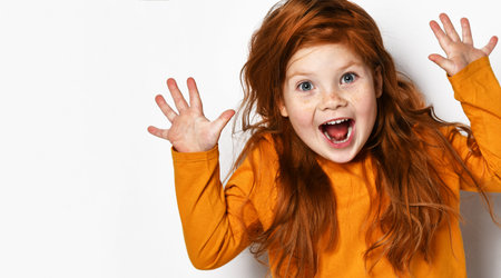 Cheerful small red haired girl with freckles in yellow comfortable longsleeve standing showing fingers and feeling excitedの写真素材