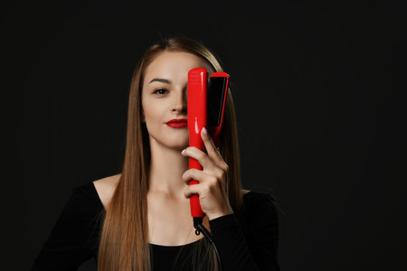 Young smiling beautiful woman with long silky straight hair in black clothes holding red hair...