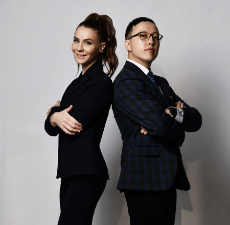 Positive man and woman business partners coworkers in official suits standing back to back with arms crossed at chestの写真素材