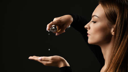 Side view. Portrait of young pretty woman pouring dropping hair cosmetics to hand for making...