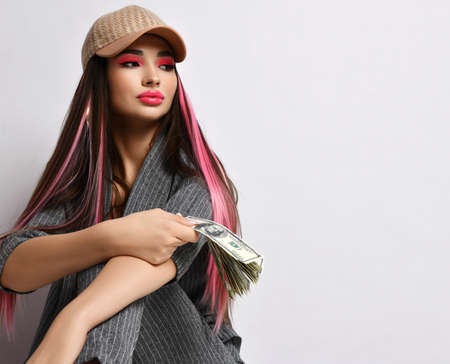 Rich pretty business woman in gray pinstripe pantsuit and cap sits at copy space holding bundle of...
