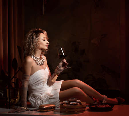 Rich wealthy blonde curly hair woman in white strapless dress is sitting on table served with...