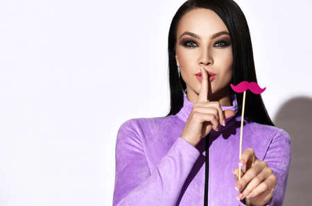 Pretty brunette woman in purple clothes gestures silence sign with finger and holding decorative...
