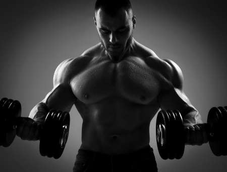 Brutal sweaty strong man athlete with naked upper body standing doing workout with dumbbels and showing strong pumped up bicepsの写真素材