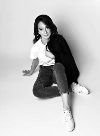 Cheerful young business woman in casual office clothing sit cross-legged on floor with her long hair over white backgroundの写真素材