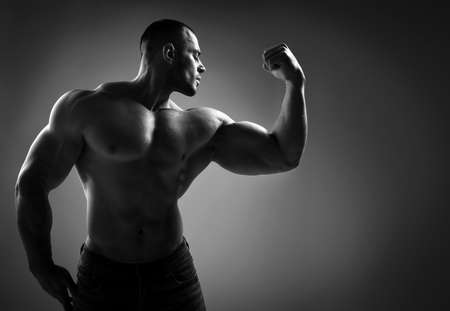 Brutal strong man athlete in jeans and half naked shirtless stands showing strong huge pumped up bicepsの写真素材