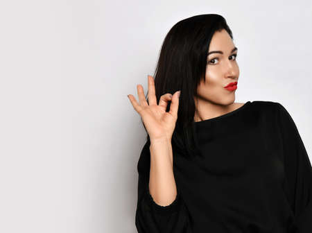 Portrait of beautiful woman in stylish casual clothing standing showing ok sign with fingers and looking at cameraの写真素材