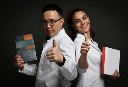 Man and woman couple doctors show thumbs up with books on dark backgroundの写真素材