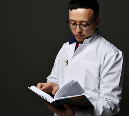 Young man doctor read book. Medicine worker. Healthcare concept on darkの写真素材
