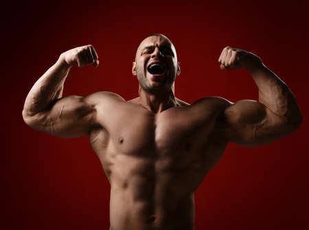 Portrait of screaming strong man, bodybuilder standing with naked chest demonstrating his muscles, biceps, chest, absの写真素材