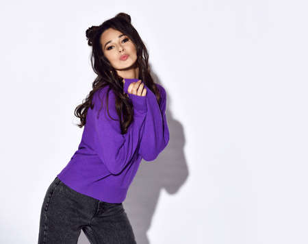 Portrait of joyful smiling romantic young pretty woman in purple pullover and jeans sending blowing a kissの写真素材