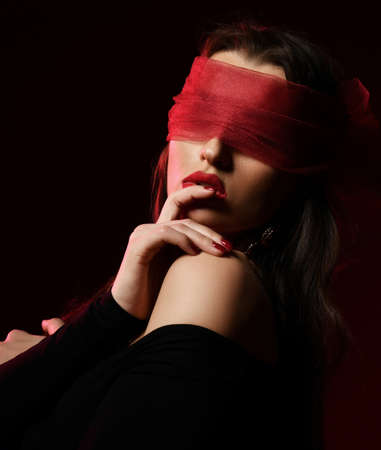 Portrait of excited brunette woman in off-shoulder dress and with eyes covered with scarf, blindfold bites her fingerの写真素材