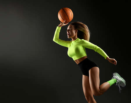 Young sexy blonde fitness woman in tight sportswear, top, shorts, high socks and sneakers jumping with basketball ballの写真素材