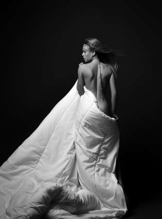 Black and white. Tall sensual sexy naked woman stands back to camera covered in large soft white blanket, looking asideの写真素材