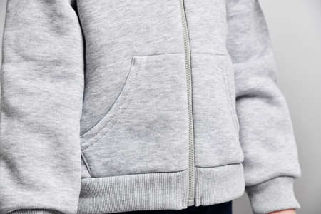 Closeup of kid girl in gray hoodie with zipper standing still holding hands down