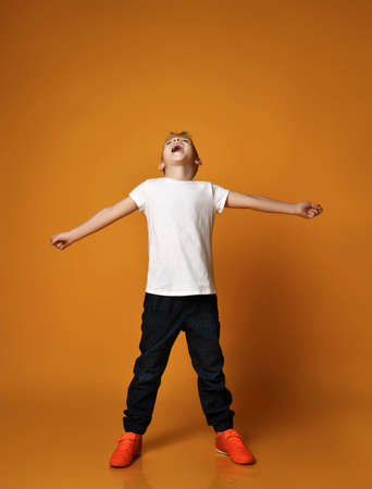 Talented kid, teenager, schoolboy in blue jeans and white blank t-shirt stands holding arms outstretched and singの写真素材