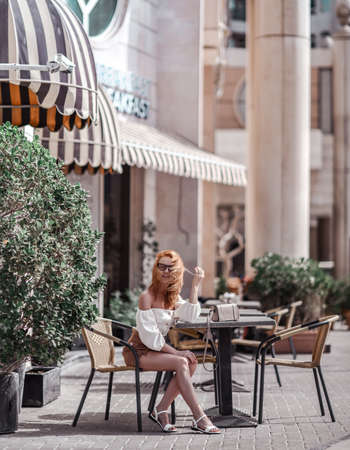 Stylish successful woman tourist in summer clothes with shorts and top blouse sits in street cafe, going to have breakfastの写真素材