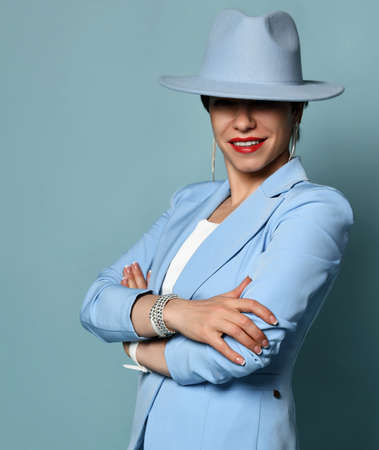 Smiling short haired brunette businesswoman in blue official suit and hat stands with arms crossed at chestの写真素材