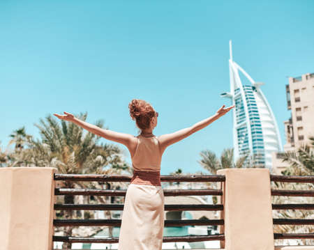 Happy beautiful unrecognizable tourist woman in summer dress stands holding hands up enjoying sightseeing in Dubaiの写真素材