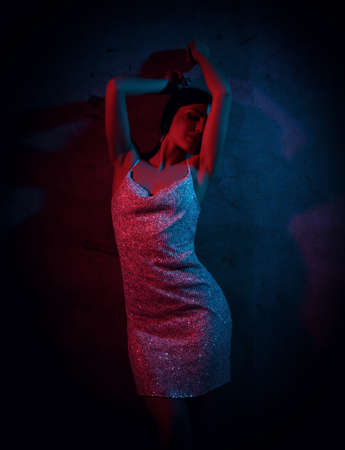 Smiling sexy beautiful young woman in silver cocktail dress standing and moving in pink and blue...