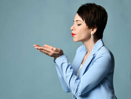 Sensual but powerful brunette businesswoman, experienced manager in blue business suit blowing something from her palmsの写真素材