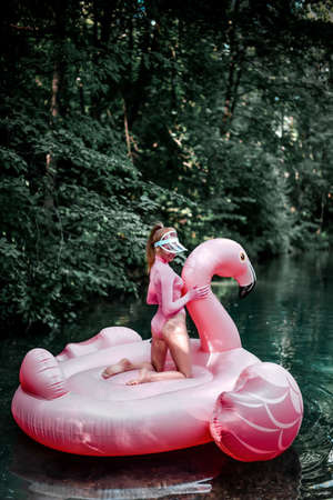 Sexy red haired woman in swimsuit floats, swims on big inflatable pink flamingo down the tropic riverの写真素材