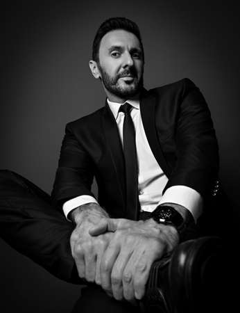 Black and white. Self-confident businessman in modern office suit sits with legs crossed looking...