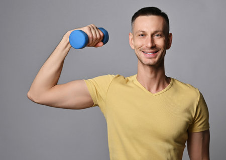 Young athletic man in t-shirt works out with weights, holds a dumbbell in hand. Healthy lifestyleの写真素材