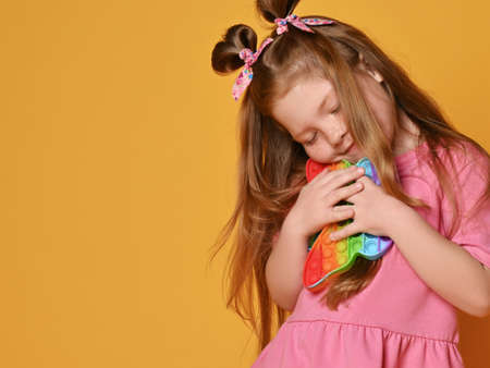 Cute red-haired kid girl in pink shirt hugs new sensory rainbow color butterfly shape toys - pop itの写真素材